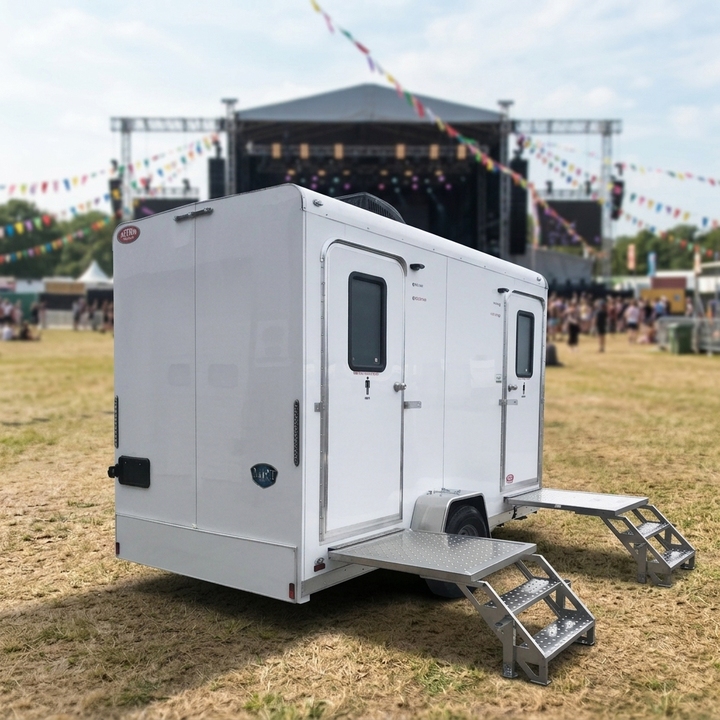 Two door washroom trailer with its entrance steps down, standing on an event field.